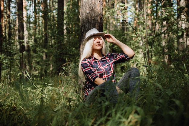 森に座っている帽子の若い大人の金髪女性
