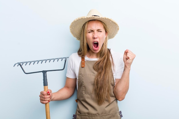 Young adult blonde woman farmer with a rake