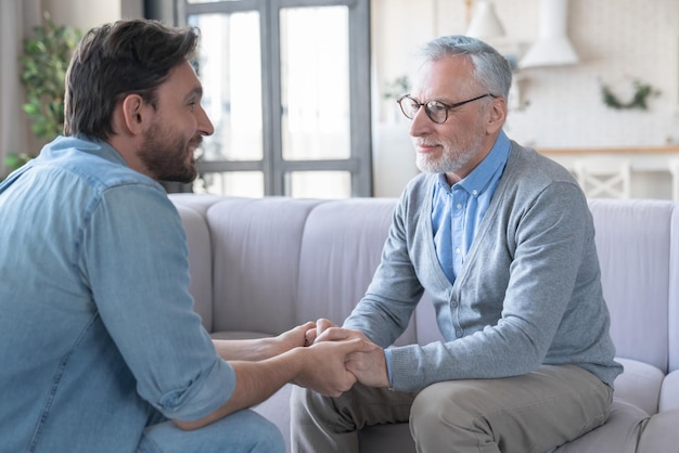 Young adult caucasian son listening and supporting his old elderly senior father at home indoorsHappy fathers day Care and love concept I love you dad