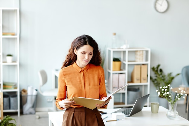 Young adult caucasian woman with long wavy hair wearing elegant orange blouse and brown skirt standi