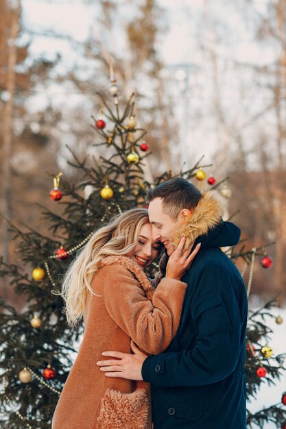 La giovane coppia adulta decora l'albero di natale nella foresta invernale il concetto di celebrazione della festa del pino di capodanno