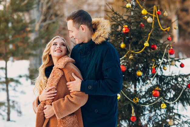 Young adult couple decorates christmas tree in winter forest. New year pine holiday party celebration concept.