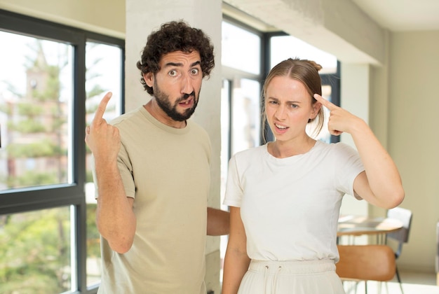 Photo young adult couple feeling confused and puzzled, showing you are insane, crazy or out of your mind