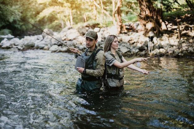 Young adult couple is fishing together on fast mountain river. Active people and sport fly fishing concept.