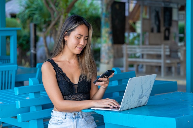 young adult east asian woman working on her laptop at a cafe at the gili air beach in indonesia