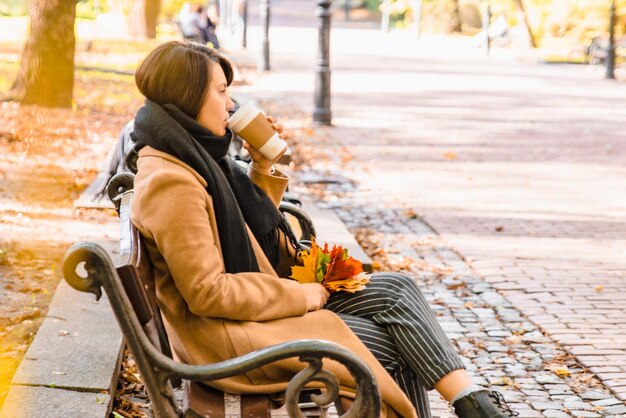 秋の秋のシーズンに都市公園のベンチに座っている若い大人のファッション女性