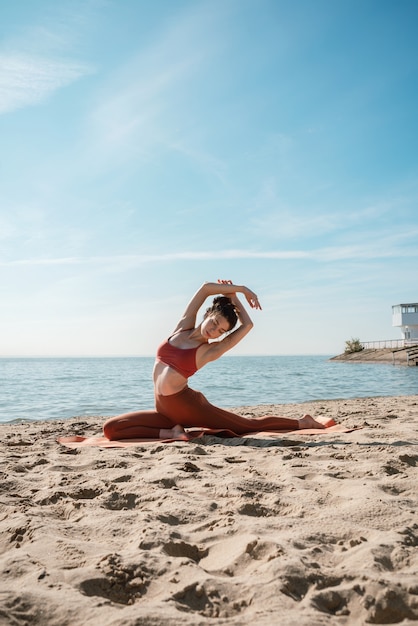 Young adult female in Pigeon pose on a beach in the morning, selective focus