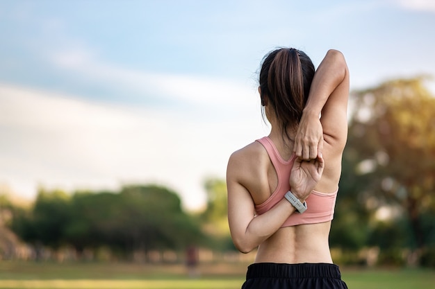 Young adult female in pink sportswear stretching muscle in the park outdoor, sport woman warm up ready for running and jogging in morning. wellness, fitness, exercise and work life balance concepts