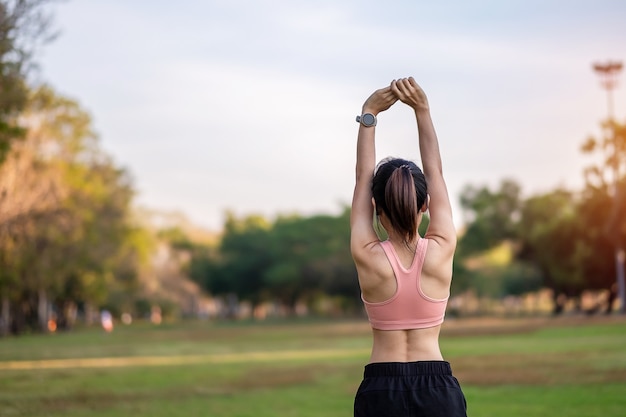 屋外の公園で筋肉を伸ばすピンクのスポーツウェアの若い大人の女性。