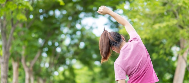 公園で筋肉を伸ばすピンクのスポーツウェアの若い成人女性
