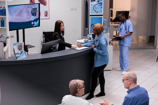 Young adult filling in registration form at hospital reception\
desk, writing medical checkup report before attending appointment.\
woman checking papers in facility lobby, having consultation.