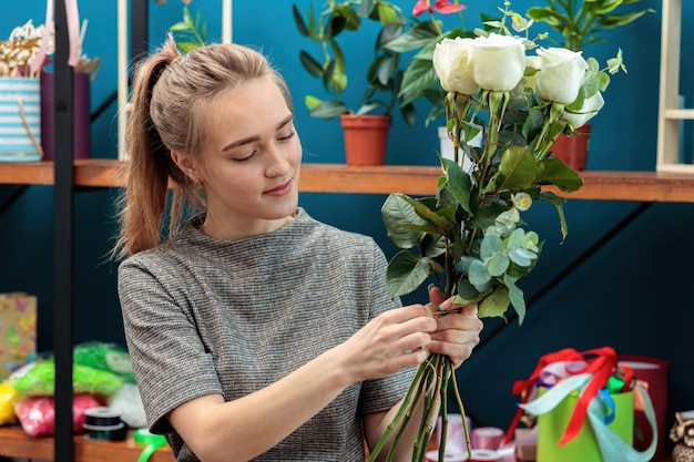 Young adult girl florist makes a bouquet of white roses.