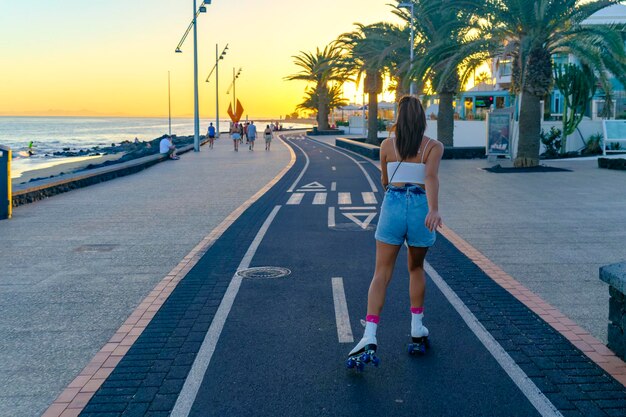 Photo young adult girl skating along the bike path on the beach boardwalk. puerto del carmen, lanzarote