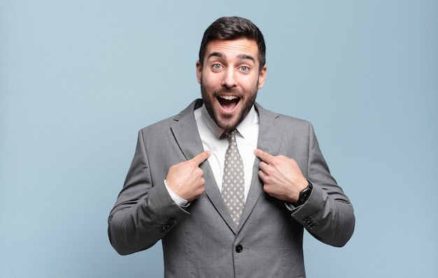 Young adult handsome businessman feeling happy, surprised and proud, pointing to self with an excited, amazed look