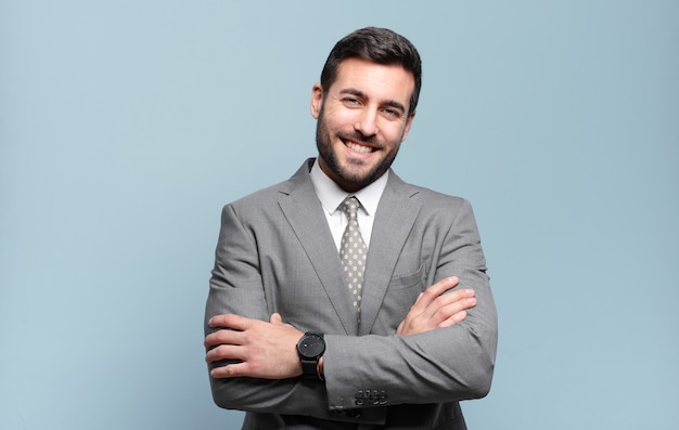 Young adult handsome businessman laughing happily with arms crossed, with a relaxed, positive and satisfied pose