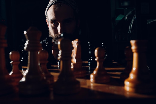 Young adult handsome man playing chess in dark with side lit