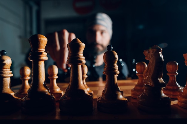Молодой взрослый красивый мужчина играет в шахматы в темноте с боковой подсветкой