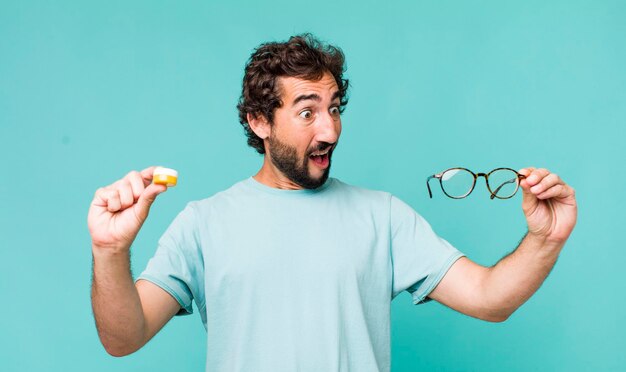 Young adult hispanic crazy man choosing between glasses or contact lens