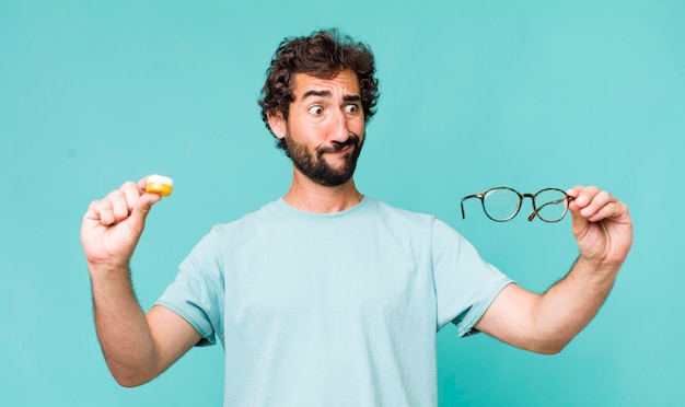 Young adult hispanic crazy man choosing between glasses or\
contact lens