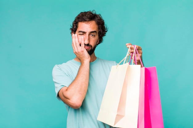 Young adult hispanic crazy man shopping bags concept