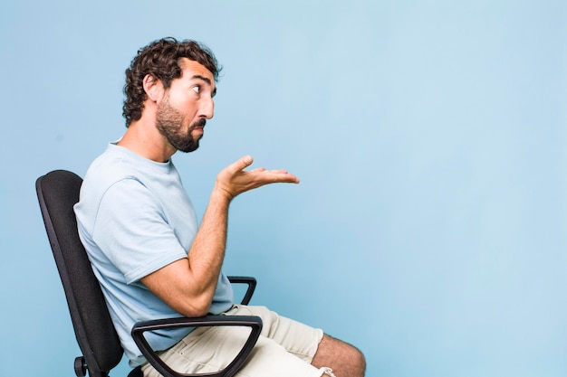 Young adult hispanic crazy man sitting on a chair copy space concept