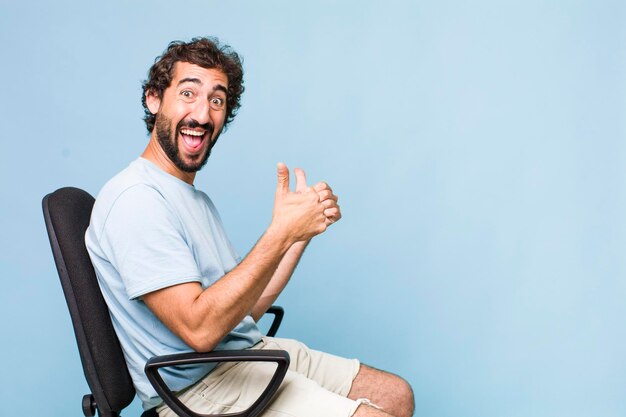 Young adult hispanic crazy man sitting on a chair copy space concept