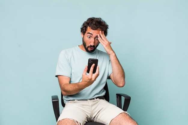 Photo young adult hispanic crazy man using his phone sitting on a chair