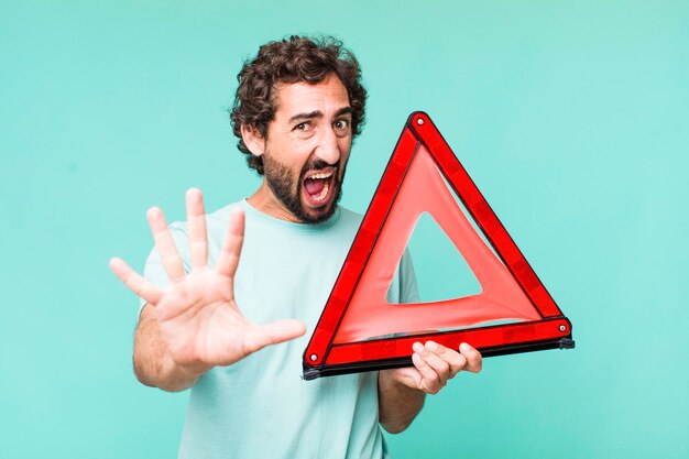 Young adult hispanic crazy man with a car emergency triangle