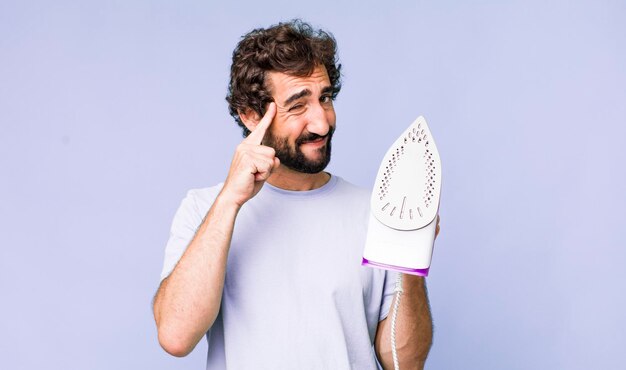 Young adult hispanic crazy man with a hand iron housework concept