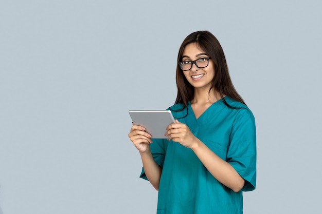 태블릿 컴퓨터 를 들고 있는 의사 의 유니폼 을 입은 젊은 성인 인도인 여자