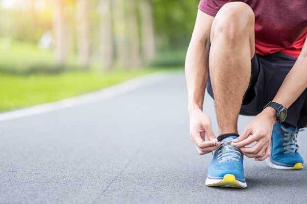 スポーツウェアと公園で靴紐を結ぶスマートウォッチの若い成人男性