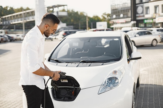 市内で電気自動車を充電している若い成人男性。エコ電気自動車のコンセプト。