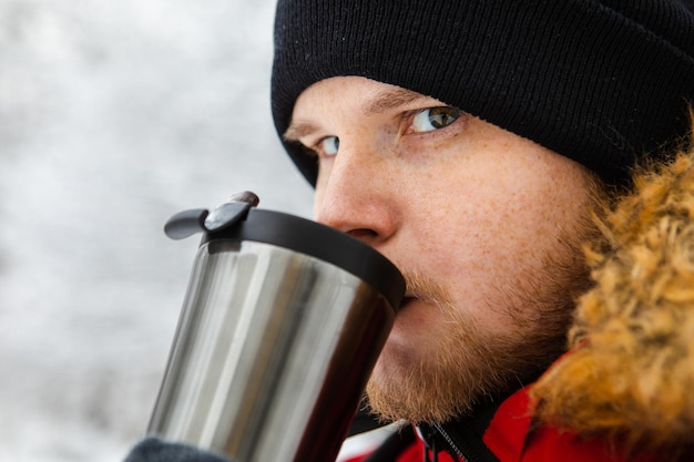 写真 屋外で詰め替え可能なマグカップからコーヒーを飲む若い成人男性