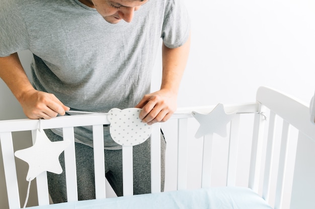 Young adult man preparing and decorating the crib for the arrival of a baby. new son concept. parenting and preparations