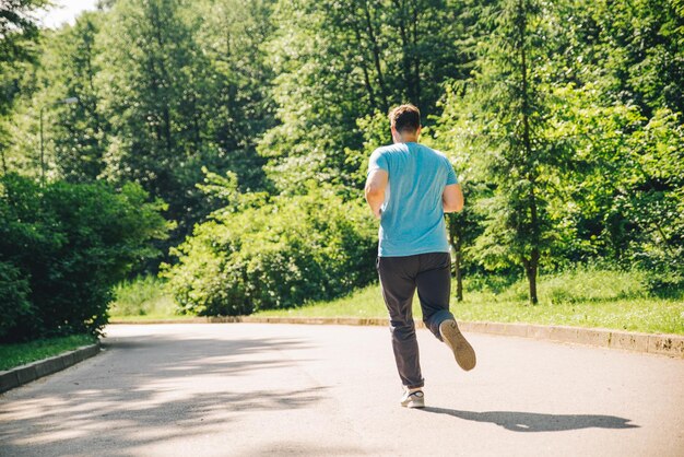 young adult man running at city park in sunny day view from behind