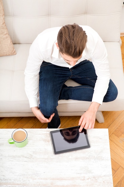 A young adult man sitting on the couch using a tablet.
