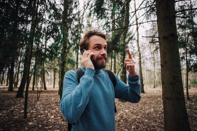 Молодой взрослый мужчина разговаривает по телефону, стоя в лесу