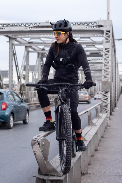 Young adult man wearing cycling equipment at urban steel\
bridge