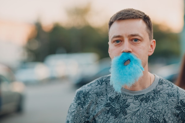 Young adult man with beard made of blue cotton candy.