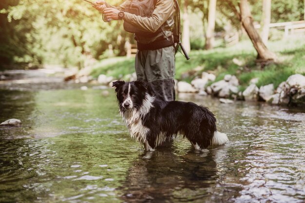 犬と一緒に若い成人男性が速い山川で釣りをしています。アクティブな人々とスポーツフライフィッシングのコンセプト。