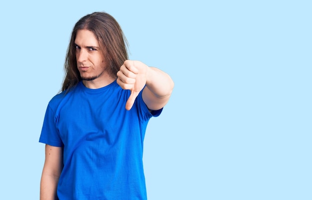 Young adult man with long hair wearing swimwear looking unhappy and angry showing rejection and negative with thumbs down gesture bad expression