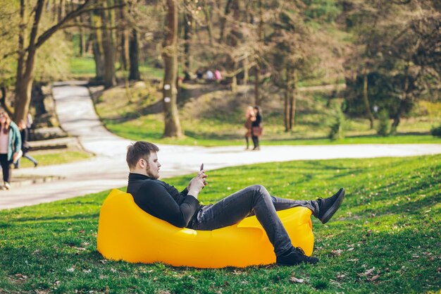 Young adult man on yellow inflatable mattress in city park