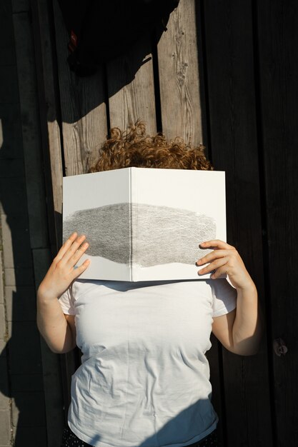 Photo young adult millennial lies on wooden planks and covers face with book summer sunny day