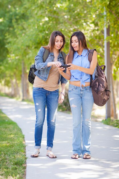 Photo young adult mixed race twin sisters sharing cell phone experience