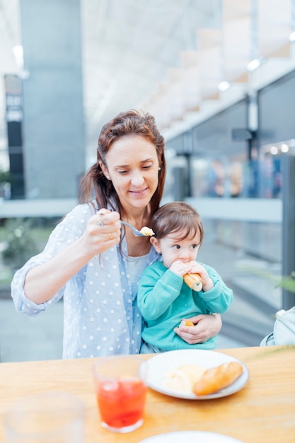 Young adult mother eating lunch with her baby in a shopping mall