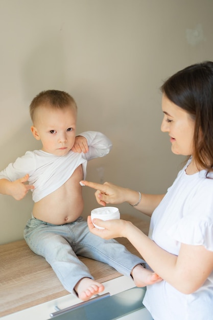 Young adult mother finger applying white medical ointment on newborn boy cheekview