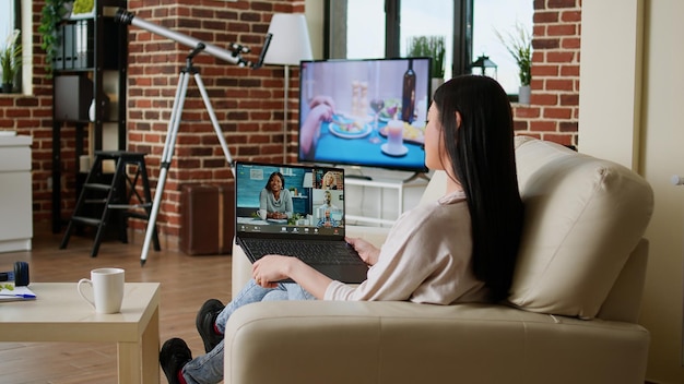 Young adult person with portable computer doing remote work\
while talking on online meeting. woman sitting on couch working\
remotely while discussing with office manager on videocall\
conference