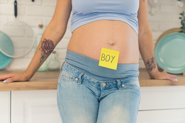 Young adult pregnant caucasian woman in mommy jeans and a crop top showing her nude belly to the