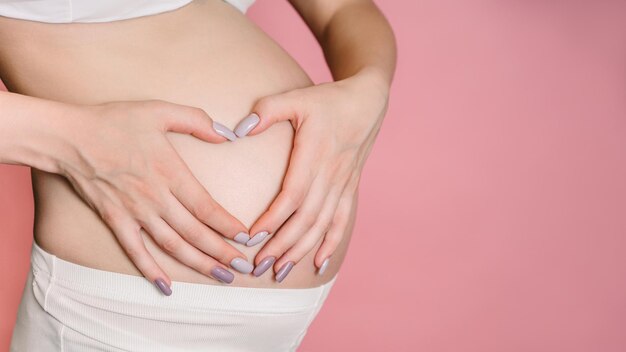 A young adult pregnant woman in white clothes touches her big naked belly with her hands