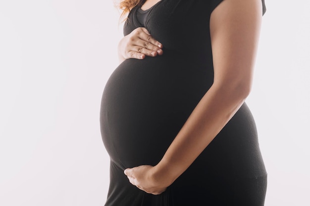 Young adult pregnant woman in white clothes touching big naked belly with hands Showing shape Pregnancy concept Expectation time Closeup Isolated on light gray wall background